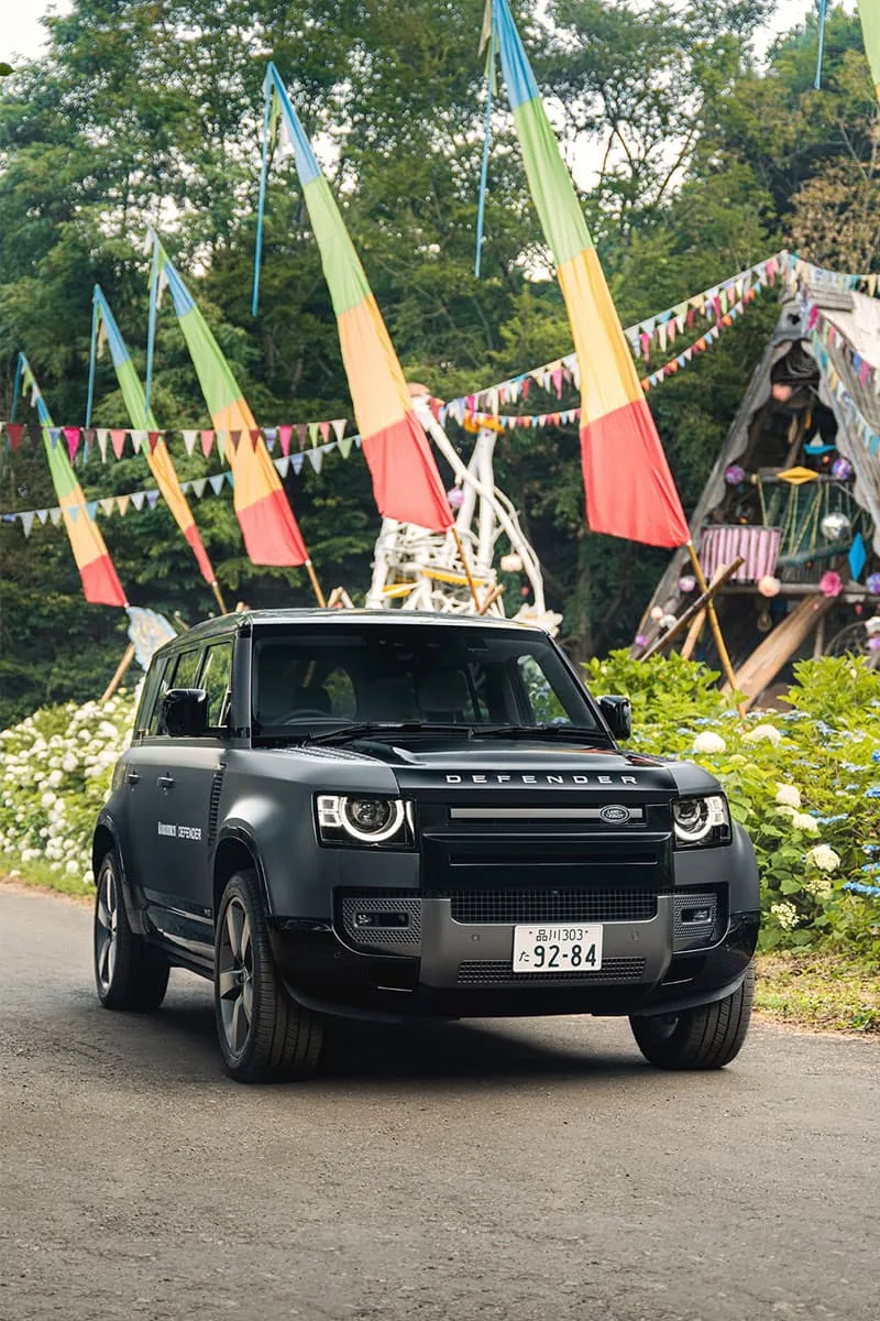 SUV noir devant décor coloré avec drapeaux et végétation luxuriante.