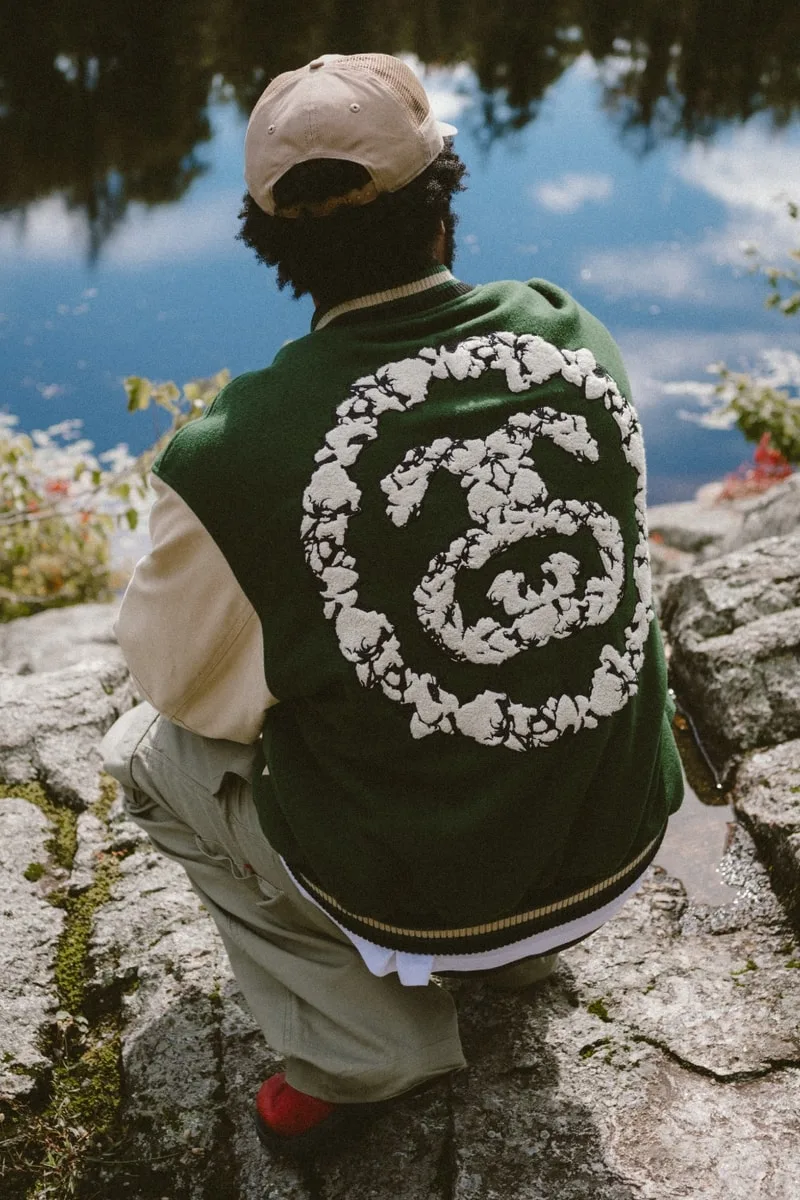 Personne assise au bord d'un lac, portant une veste verte avec motif blanc au dos.