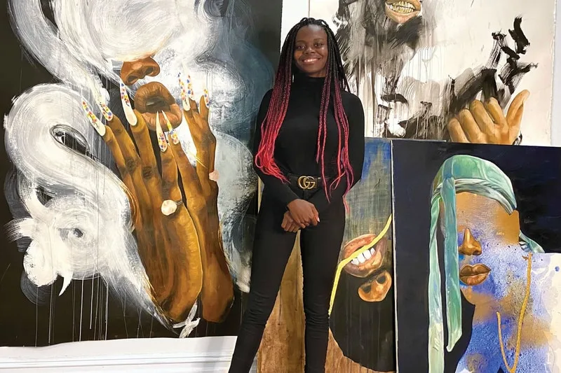 Femme posant devant des peintures colorées et abstraites.