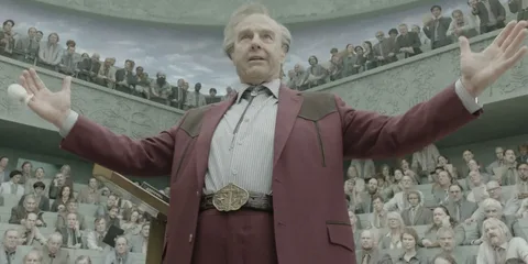 Homme en costume bordeaux parlant devant une assemblée.