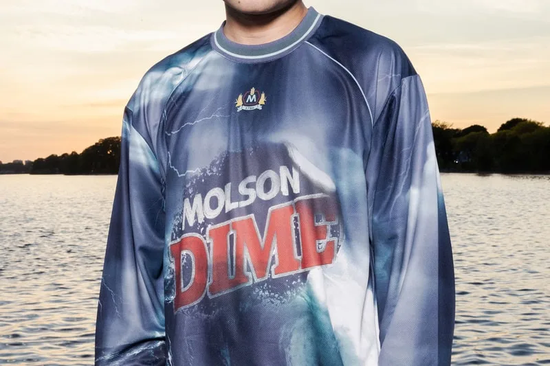 Homme en maillot 'Molson Dime' devant un lac au crépuscule.