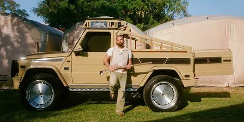 Homme posant devant un camion beige modifié avec fusil.