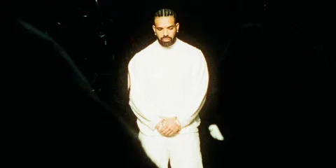 Homme en blanc sur fond sombre avec les bras croisés.