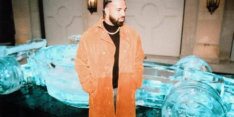 Homme en manteau brun devant sculpture voiture en glace