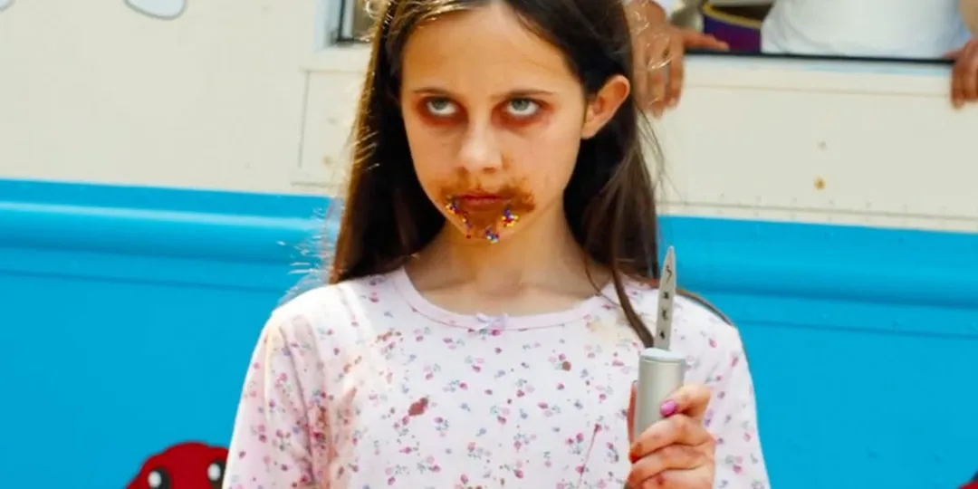 Fille avec du chocolat autour de la bouche tenant un couteau devant un camion de glace.
