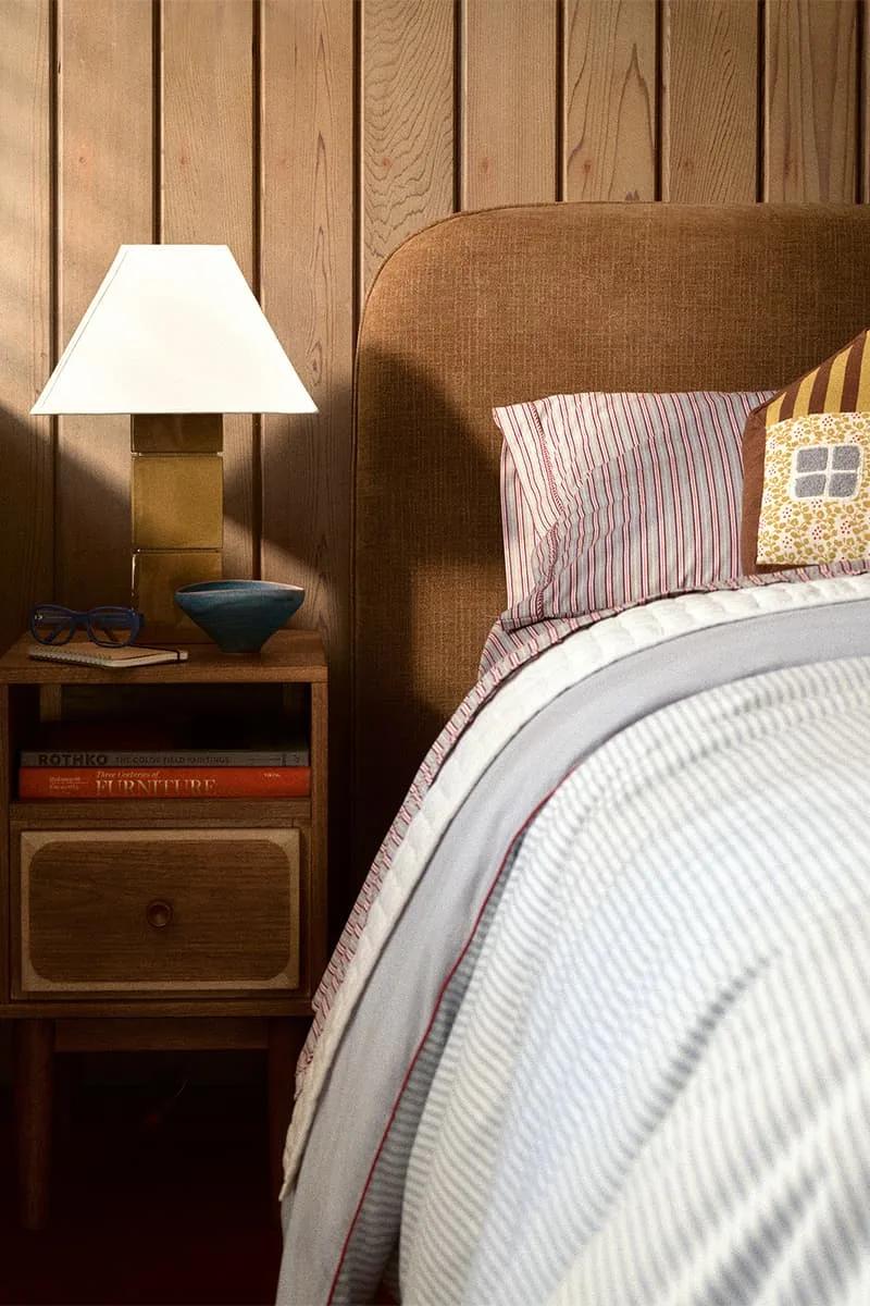 Chambre avec lampe sur table de chevet et lit aux draps rayés