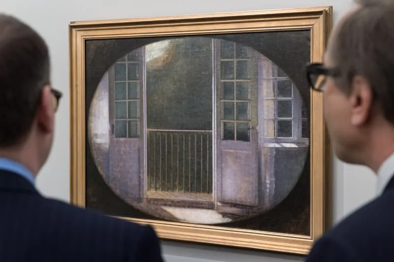 Deux hommes regardent une peinture de portes ouvertes sur un balcon vide dans un cadre ovale.