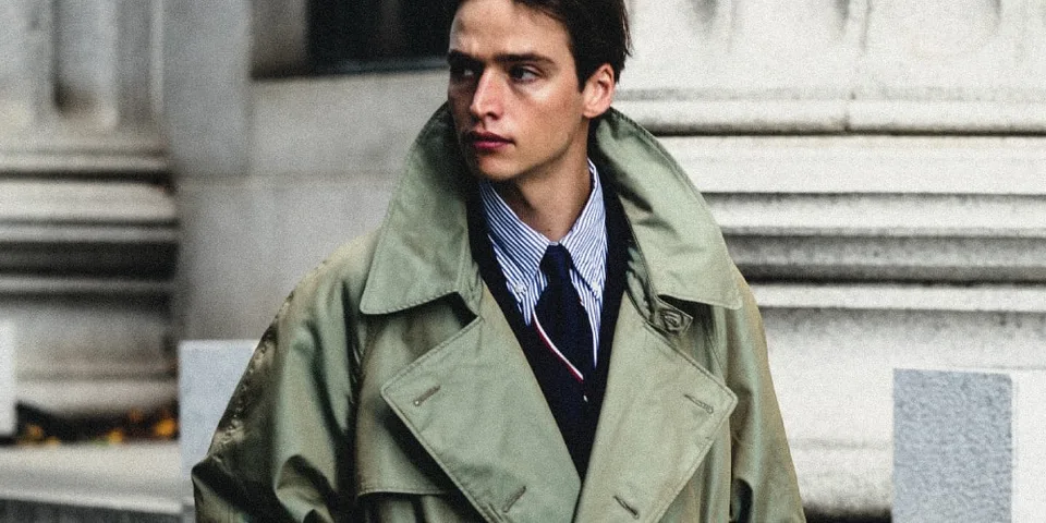 Homme en trench-coat beige, chemise rayée et cravate noire.