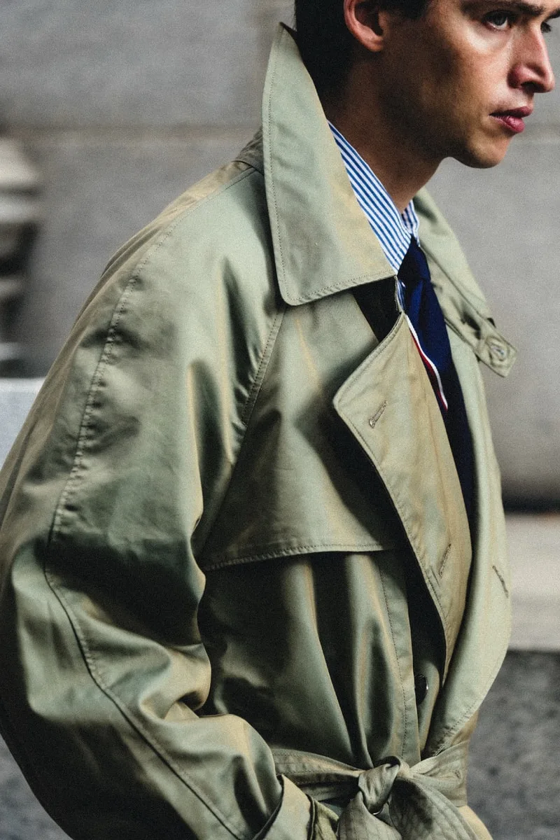 Homme en trench beige, vue de profil, portant une chemise rayée et une cravate.