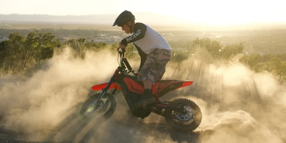Homme en motocross électrique dans la poussière au coucher du soleil.