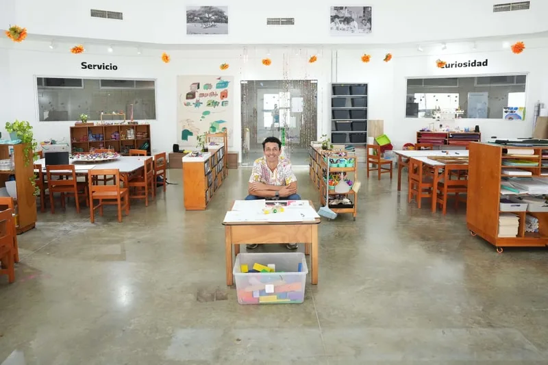 Homme assis dans une salle de classe avec des tables et des chaises en bois.
