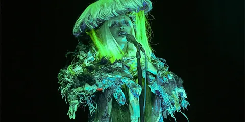 Personne avec tenue extravagante et perruque lumineuse sur scène.
