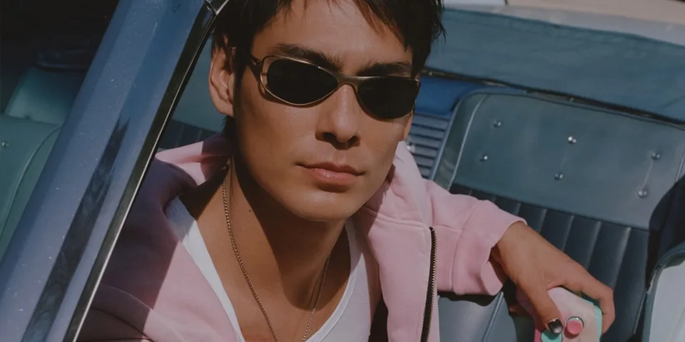 Homme en lunettes de soleil dans une voiture, portant une veste rose.