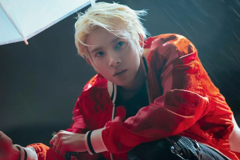 Personne en veste rouge sous un parapluie transparent avec éclairage dramatique.