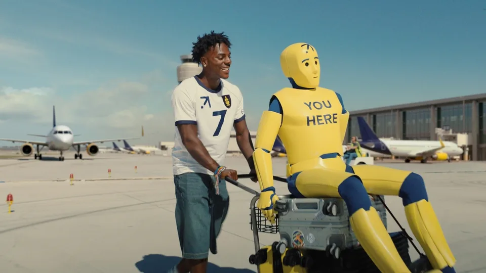Homme poussant un mannequin crash test sur chariot à l'aéroport.