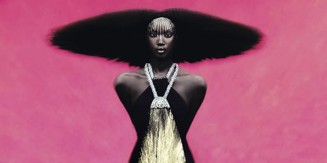 Mannequin à la coiffure afro spectaculaire et au collier doré sur fond rose.