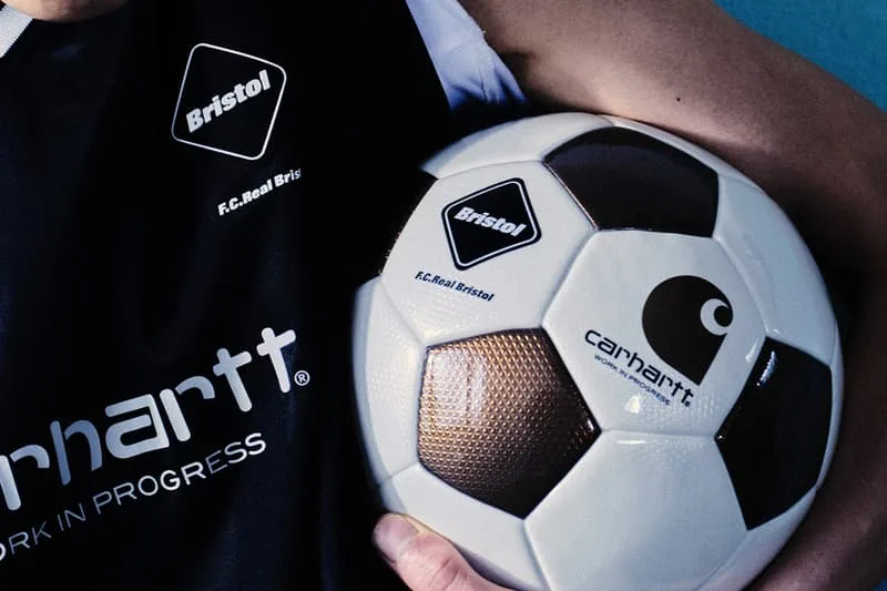 Personne tenant un ballon de football avec logos Carhartt et Bristol.