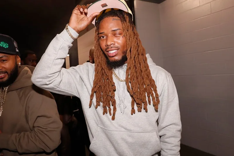 Homme avec dreads souriant, portant un sweat à capuche gris.