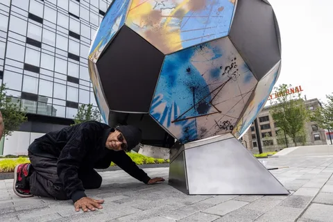 Homme et sculpture géométrique colorée en extérieur urbain.