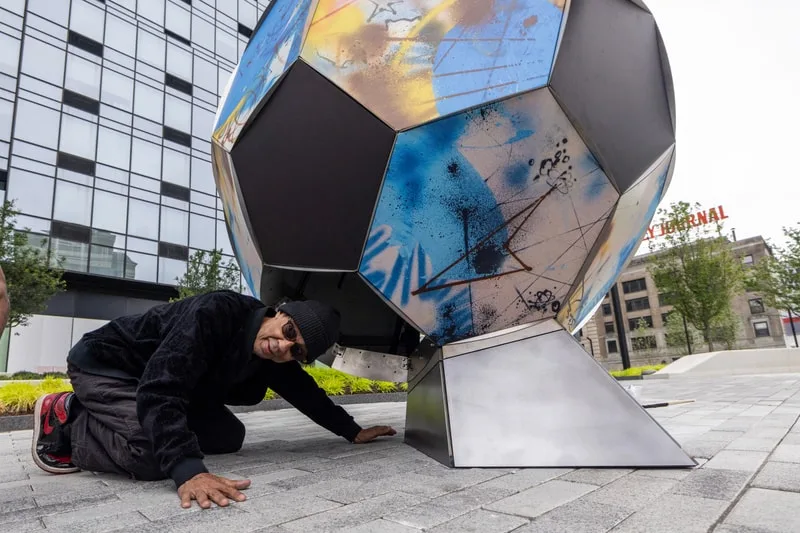 Homme et sculpture géométrique colorée en extérieur urbain.
