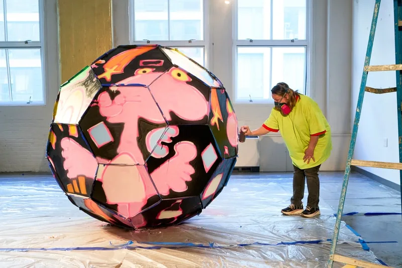 Artiste peignant un grand polyèdre coloré dans une pièce lumineuse.