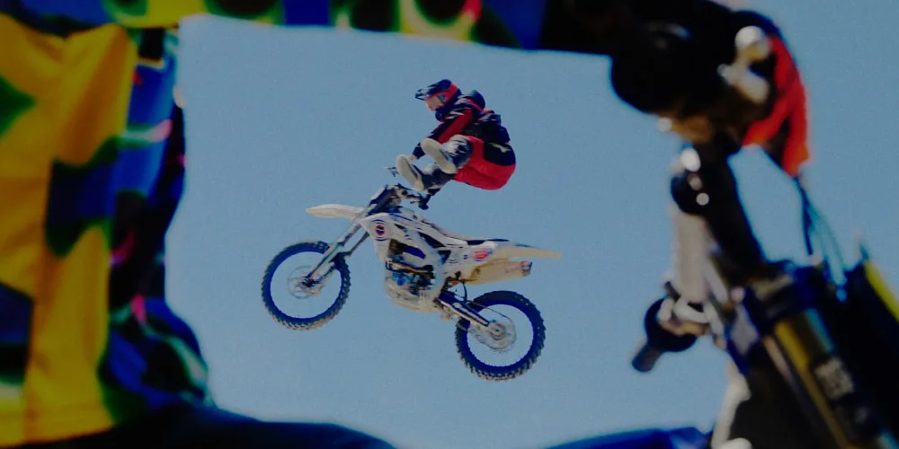 Motard en plein saut avec un fond de ciel bleu, encadré par une autre moto.