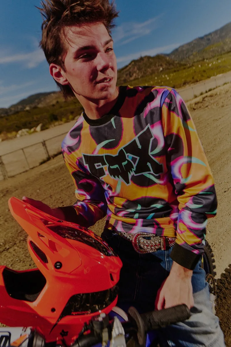 Motard avec casque rouge et pull coloré sur une piste de terre.