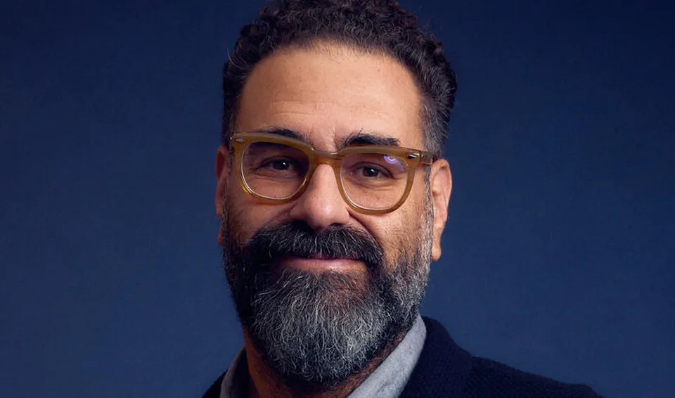 Homme avec lunettes et barbe, fond bleu sombre.