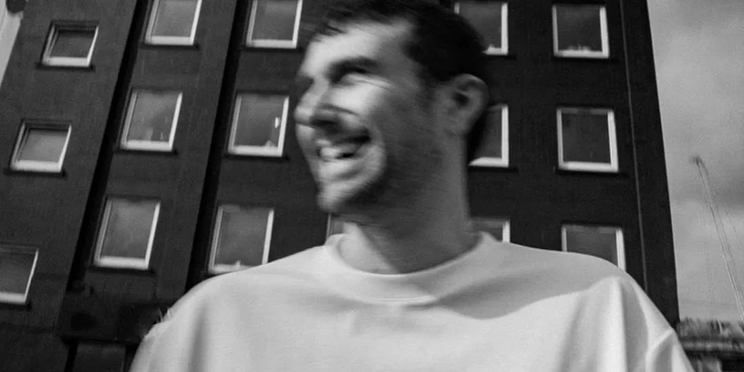 Homme flou souriant devant un immeuble en arrière-plan.