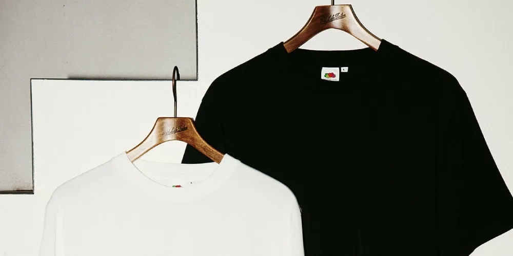Deux t-shirts suspendus, un noir et un blanc, sur des cintres en bois.