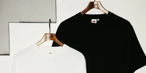 Deux t-shirts suspendus, un noir et un blanc, sur des cintres en bois.