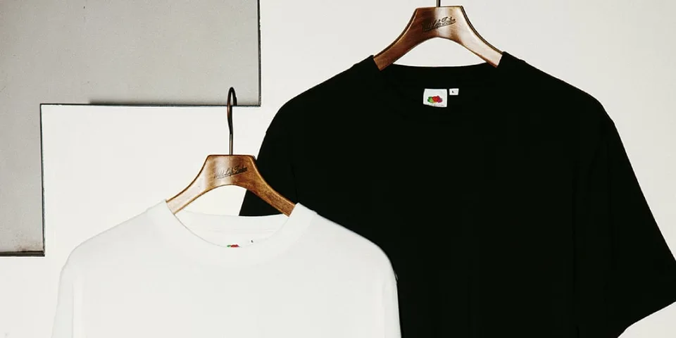 Deux t-shirts suspendus, un noir et un blanc, sur des cintres en bois.
