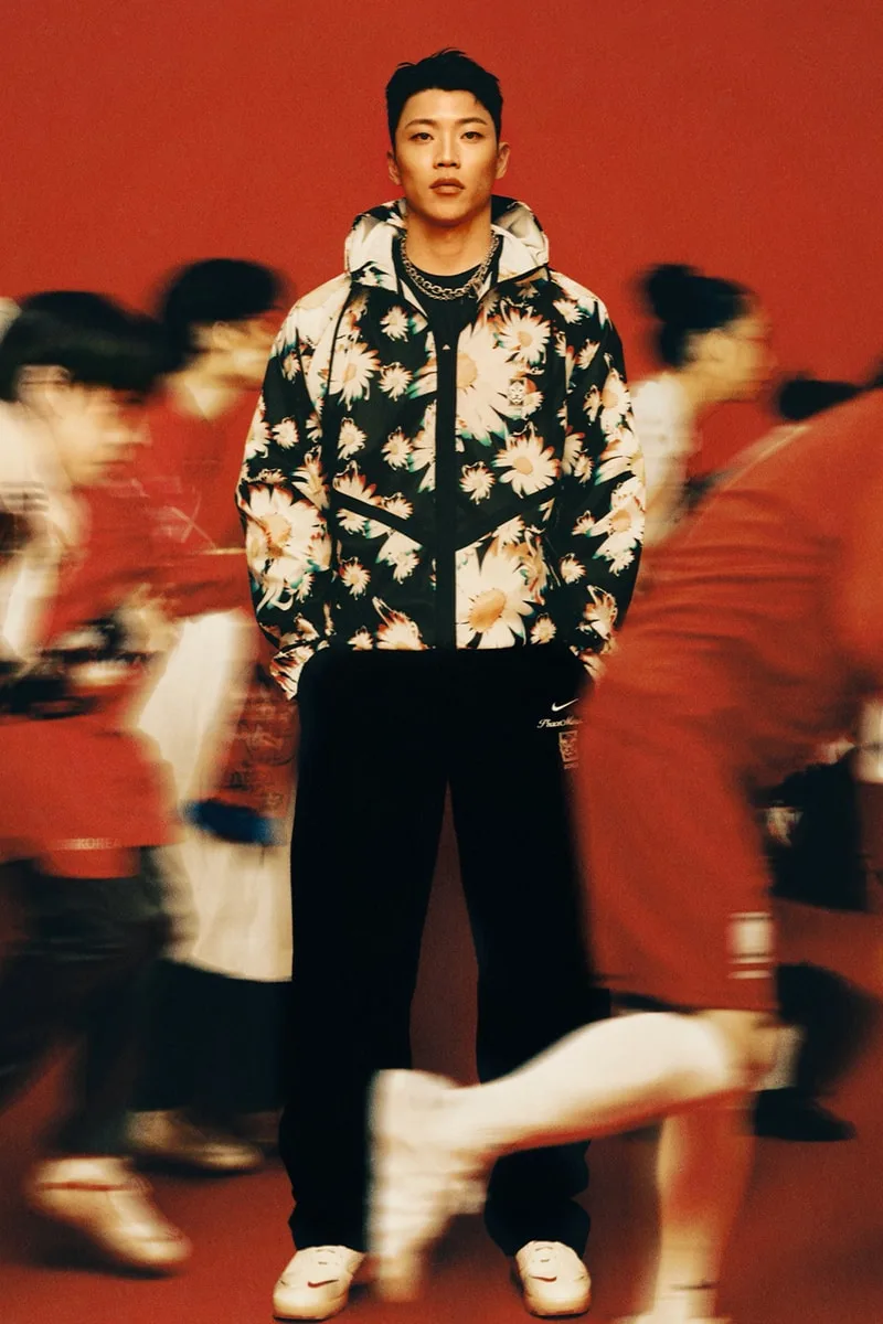 Homme en veste à fleurs sur fond rouge, entouré de personnes floues.