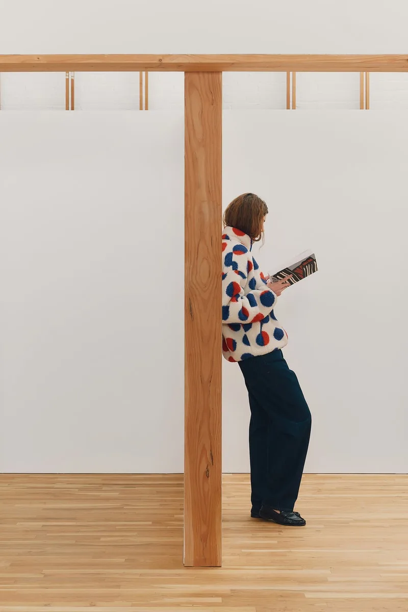 Personne lisant un magazine appuyée contre un poteau en bois.