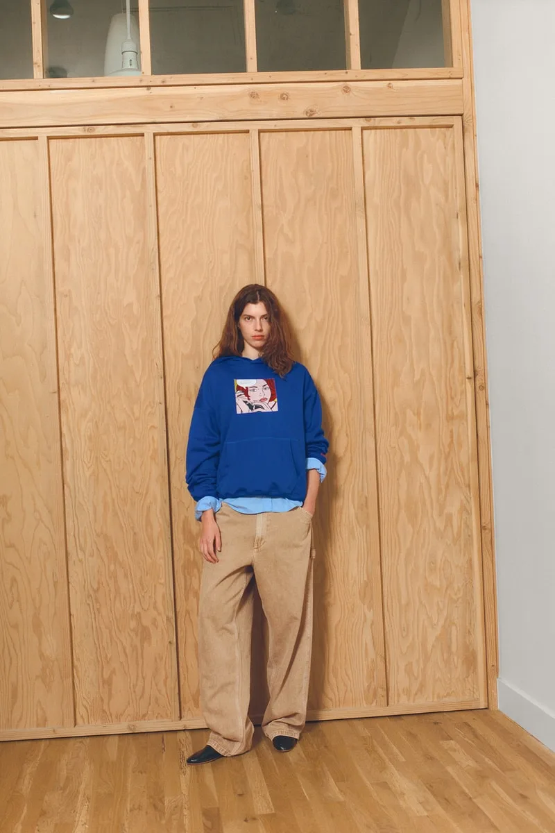 Personne avec sweat bleu et pantalon beige devant un mur en bois.
