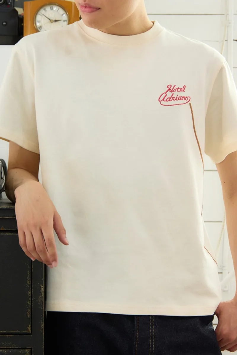 Homme en t-shirt blanc avec texte 'Hotel Adriano' en rouge.