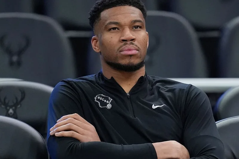 Homme assis en sweat noir Nike avec logo Bucks, bras croisés.