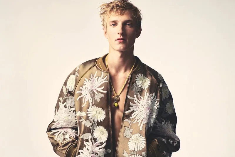 Homme en veste à motifs floraux, posant debout.