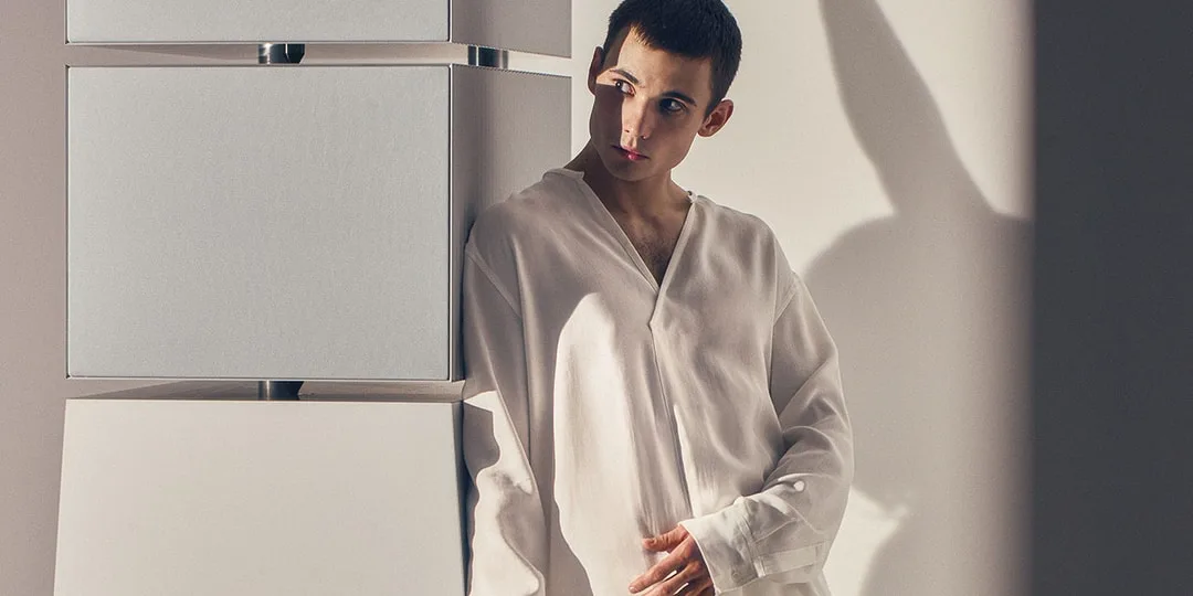 Homme en chemise blanche s'appuyant contre des structures géométriques.