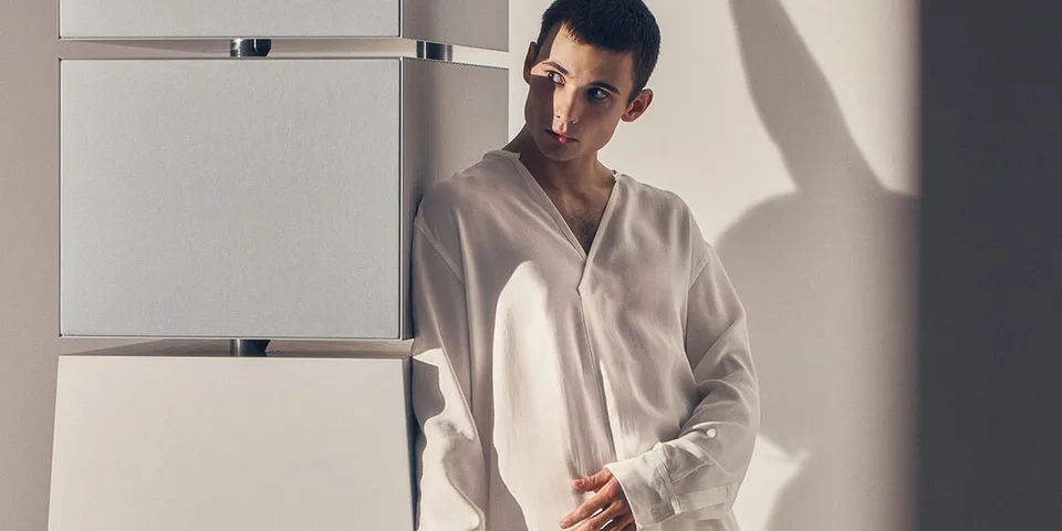 Homme en chemise blanche s'appuyant contre des structures géométriques.