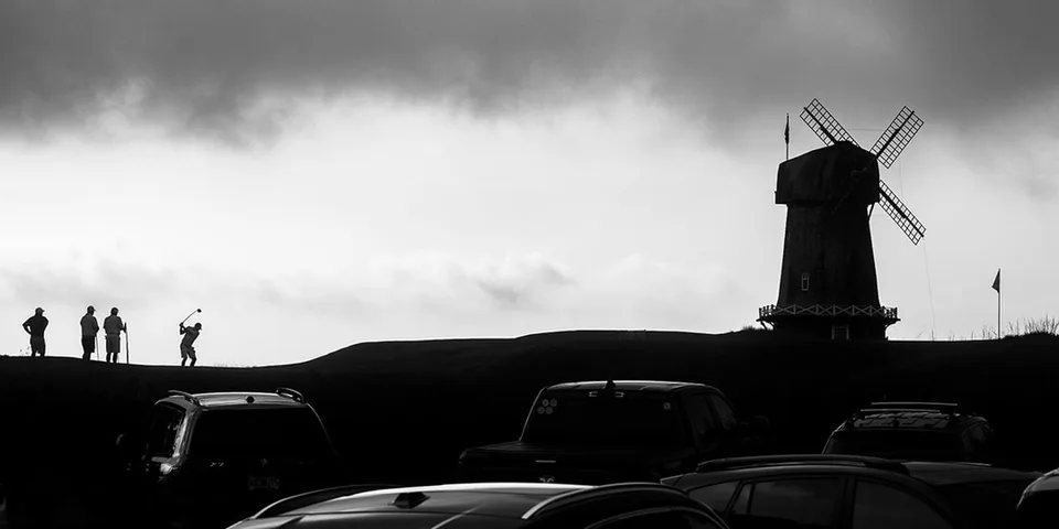 Silhouette d'un moulin à vent, golfeurs et voitures au premier plan.