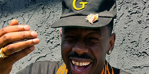Homme souriant avec une casquette et un grillz doré.