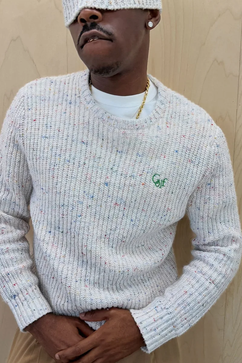 Homme portant un pull en maille gris avec un logo vert.