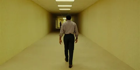 Personne marchant dans un long couloir jaune avec une autre silhouette au loin.