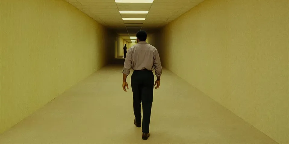 Personne marchant dans un long couloir jaune avec une autre silhouette au loin.