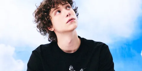 Jeune homme aux cheveux bouclés regardant vers le ciel, fond bleu et nuages