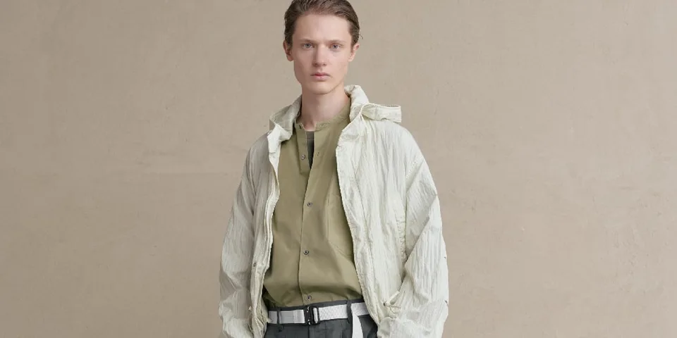 Homme en veste beige et chemise kaki sur fond beige.