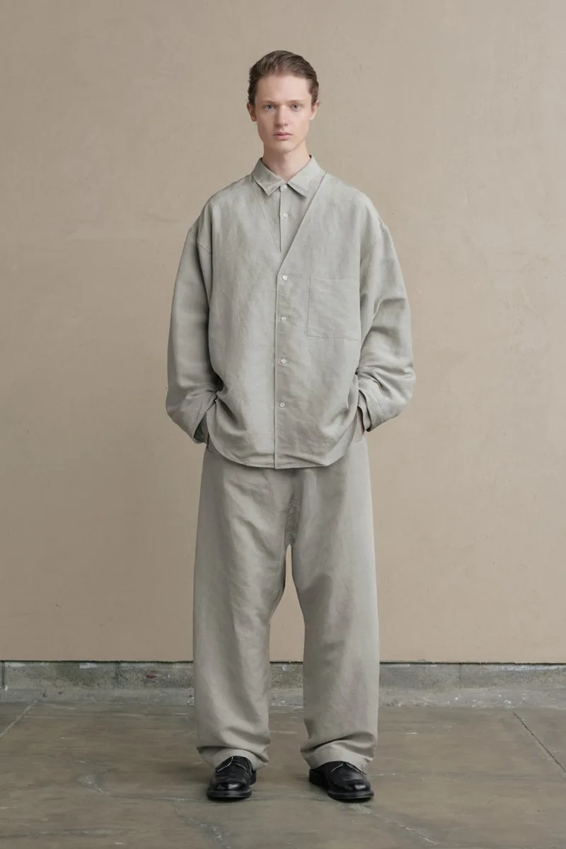 Homme en vêtements amples couleur beige, pose contre un mur beige.