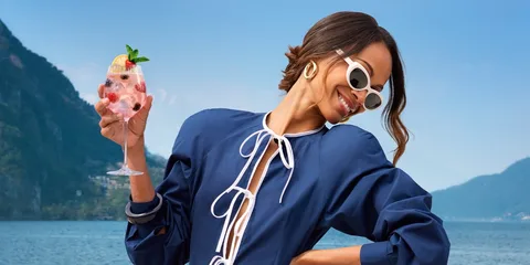 Femme avec lunettes de soleil tenant une boisson, paysage montagneux en arrière-plan