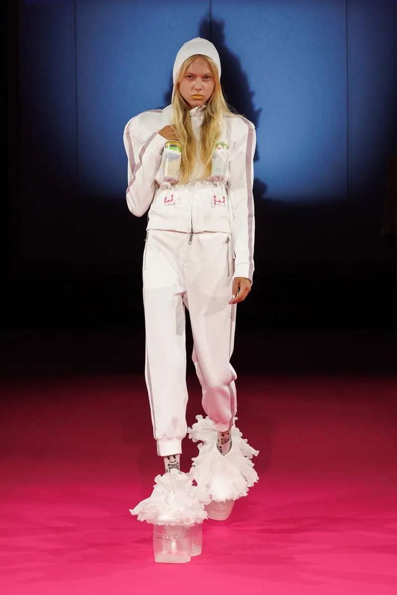 Modèle en tenue blanche sur podium rose avec chaussures originales.